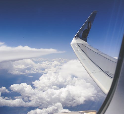 晴朗的蓝天下云层上方飞机机翼的高角度照片 · 免费素材图片