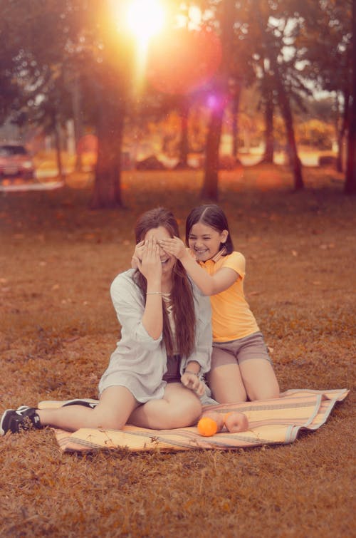 两个女人在日落时分坐在棕色的野餐垫上 · 免费素材图片