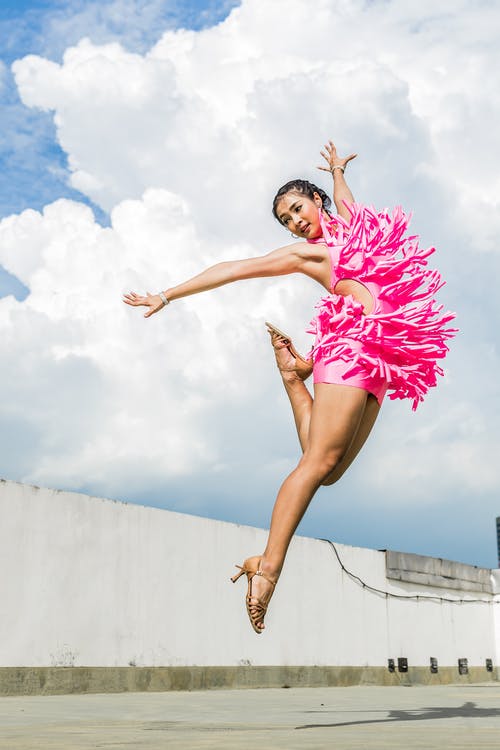 粉红色的连衣裙，做着跳投，同时在白云下伸胳膊的女人 · 免费素材图片