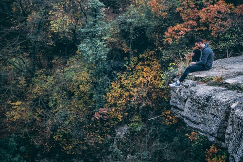 坐在岩石悬崖上的连帽衫的男人 · 免费素材图片