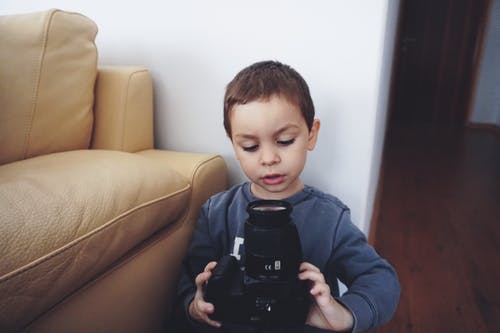 男孩抱着黑色的数码单反相机 · 免费素材图片