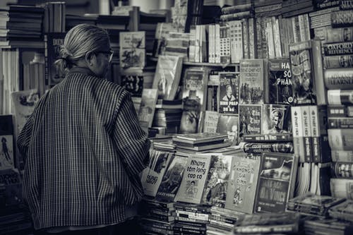 站在灰度摄影的各式各样的书前的人 · 免费素材图片