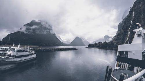 多云的天空下水面上游艇的灰度照片 · 免费素材图片
