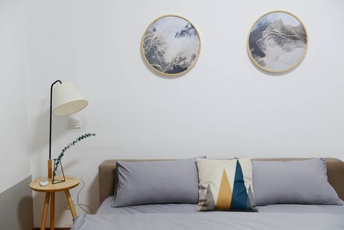 米色木制床头柜，带白色台灯；棕色木制床和灰色床罩套 · 免费素材图片