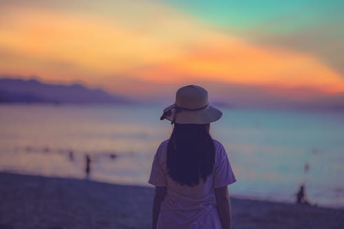 白色礼服站在日落海滩附近的女人 · 免费素材图片
