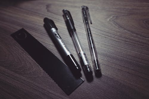 三支圆珠笔和米色木质表面上的黑色标尺 · 免费素材图片