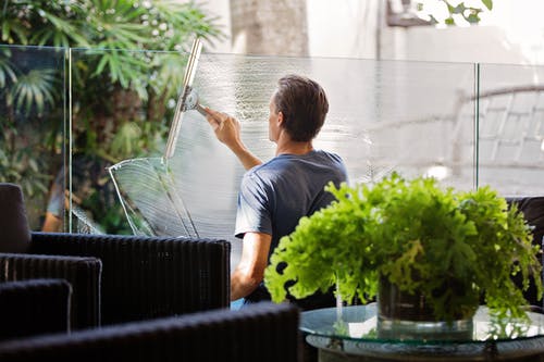 灰色衬衫清洗沙发附近的透明玻璃墙的男人 · 免费素材图片