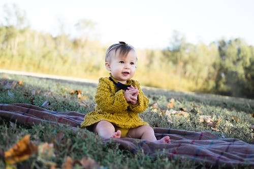 婴儿穿着黄色钩针编织的长袖连衣裙坐在棕色纺织 · 免费素材图片