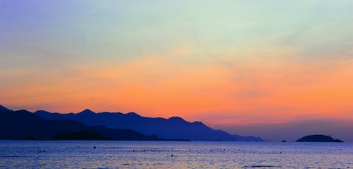 橙色日落期间海洋旁边山的轮廓 · 免费素材图片