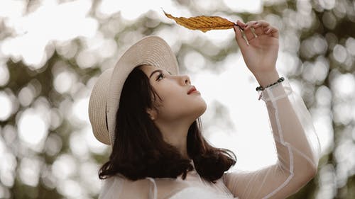 女人拿着棕色的叶子的时候穿着白色的长袖勺脖子上衣 · 免费素材图片