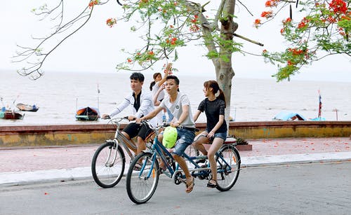 两个男孩和一个女孩在水体旁边的道路上骑自行车 · 免费素材图片