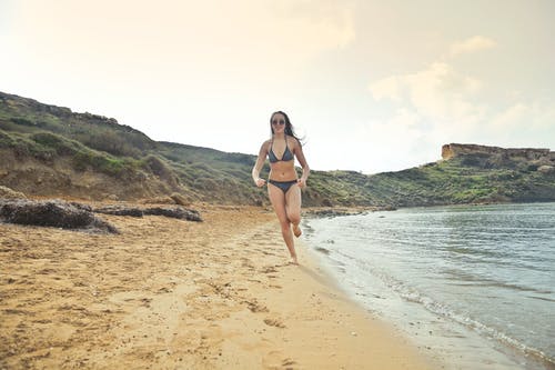 女人穿着灰色比基尼在白色的沙滩上运行 · 免费素材图片