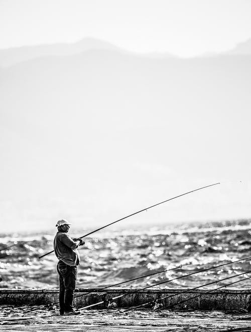 站在海边拿着钓鱼竿在灰度摄影附近的人 · 免费素材图片