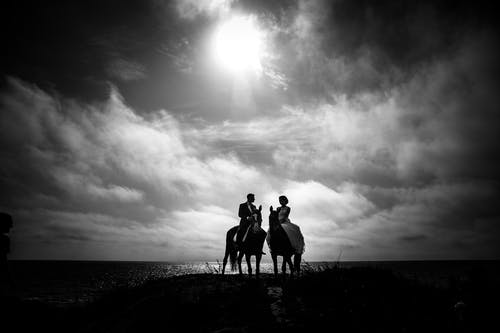 夫妇骑马以水和天空为背景的灰度摄影 · 免费素材图片