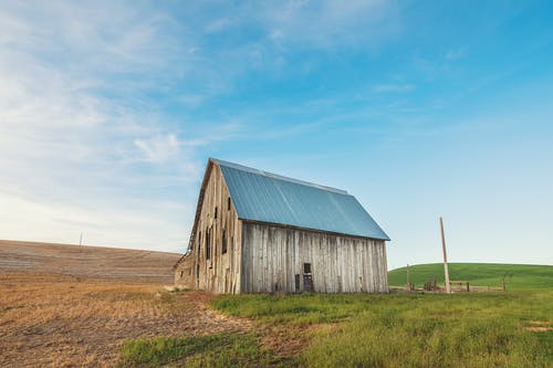 米色和灰色木制谷仓房子在绿色草地上的照片 · 免费素材图片