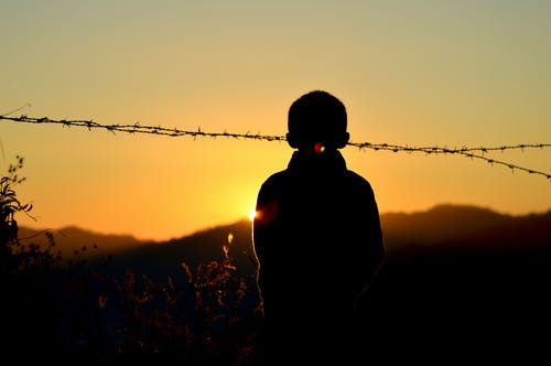 黄金时段站在铁丝网围栏附近的男孩的身影 · 免费素材图片