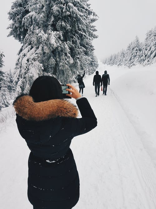 穿黑大衣的女人在雪地里散步时在她面前拍三个人的照片 · 免费素材图片