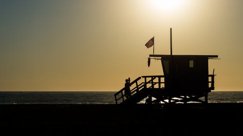 日落期间海洋附近的救生员房子的轮廓 · 免费素材图片