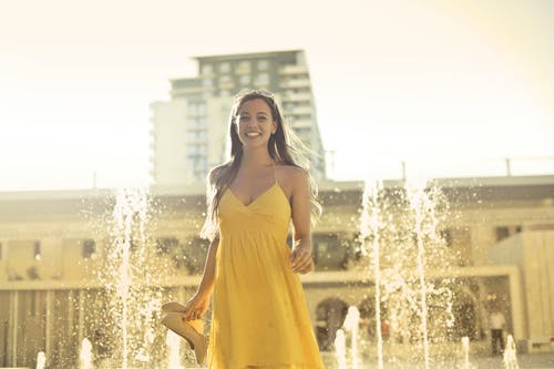 女人穿着黄色意大利面条皮带礼服站在喷泉附近 · 免费素材图片