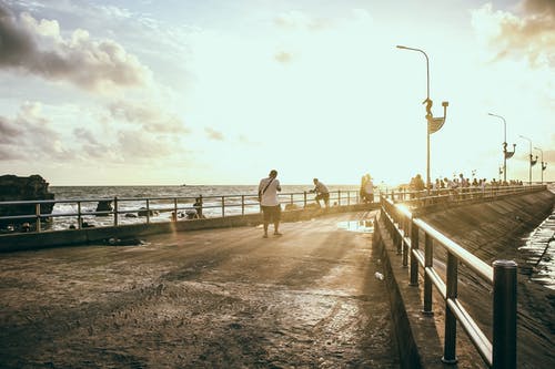 男人穿着白衬衫在海边的混凝土路面上行走 · 免费素材图片