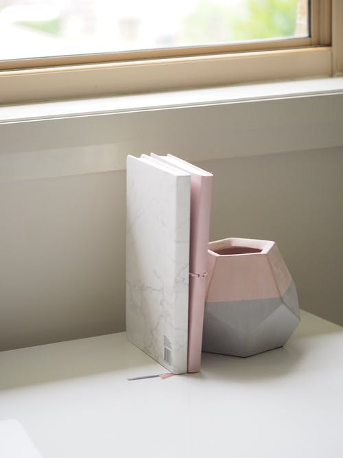 白色和粉红色的书，堆放在粉红色和灰色的陶瓷花瓶旁边 · 免费素材图片