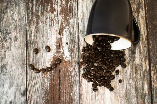 黑色的陶瓷杯，咖啡豆全部在褐色的木质表面上 · 免费素材图片