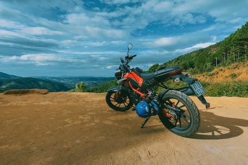 悬崖附近的橙色和黑色运动摩托车的摄影 · 免费素材图片