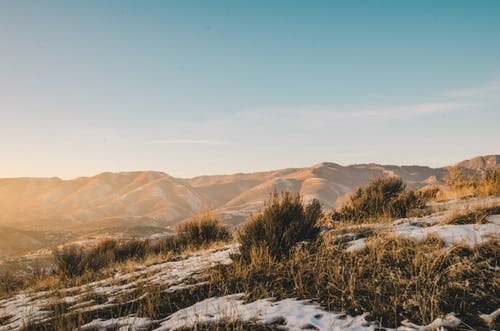 绿色和棕色草覆盖着雪，俯瞰布朗山和山脉在晴朗的蓝天下白天 · 免费素材图片