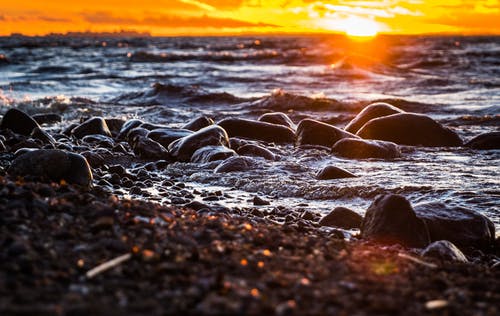 日落期间被水体包围的石头 · 免费素材图片