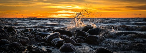 日落期间在海滩上的石头溅起的海浪 · 免费素材图片
