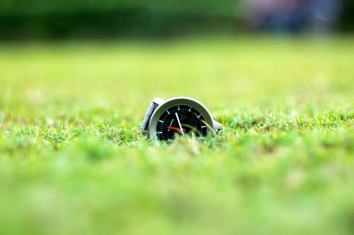 在绿色草地上的圆形灰色和黑色模拟手表 · 免费素材图片