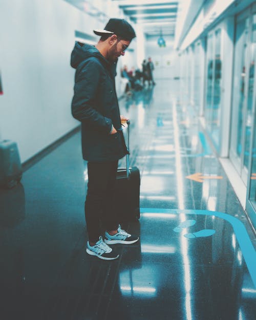 男子拿着行李站在玻璃面板的前面 · 免费素材图片