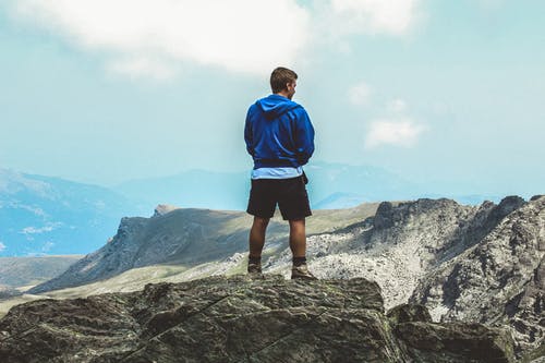 身穿蓝色连帽衫站在山顶上的男人 · 免费素材图片