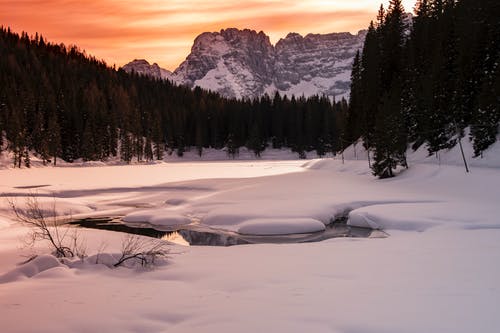 被白雪覆盖，被树木和山包围的水体的风景摄影 · 免费素材图片