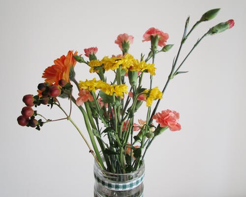 透明玻璃花瓶，红色和黄色的花朵 · 免费素材图片