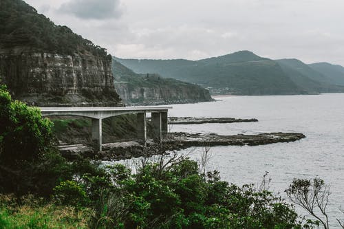 在多云的天空下海岸线上方山附近的混凝土桥梁 · 免费素材图片