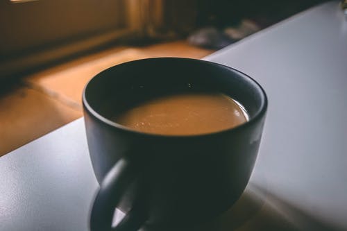 浅咖啡色的黑色陶瓷杯，桌上装满棕色咖啡 · 免费素材图片