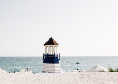 海滩附近的蓝色和白色彩绘的灯塔照片 · 免费素材图片