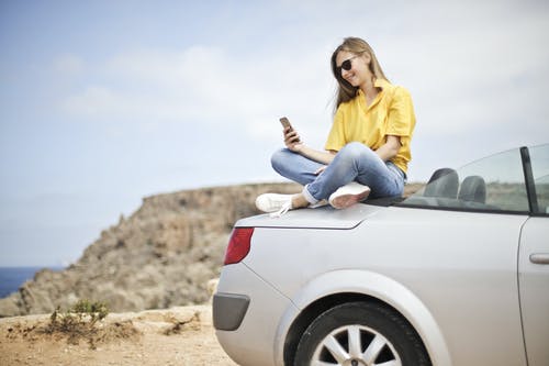 黄色上衣和蓝色牛仔裤，坐在车上采取自拍照的女人 · 免费素材图片