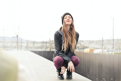 女人穿着灰色连帽外套蹲下姿势的选择性照片 · 免费素材图片