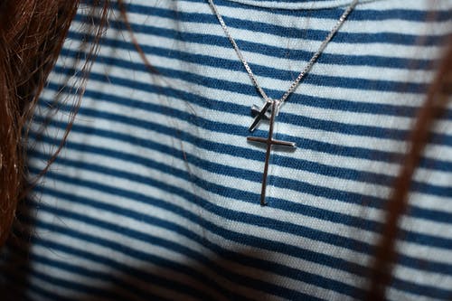 黑色和白色条纹纺织品上的银色十字架吊坠 · 免费素材图片