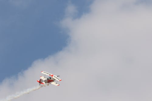 白色和红色的双翼飞机在白阴天期间飞行 · 免费素材图片