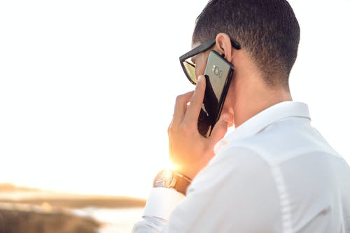 浅色摄影的一个人，穿着白领礼服衬衫，使用黑色android智能手机与电话交谈 · 免费素材图片