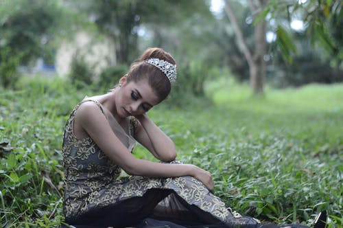 女人穿着棕色和白色的无袖花绣的裙子，坐在绿色的草地上 · 免费素材图片