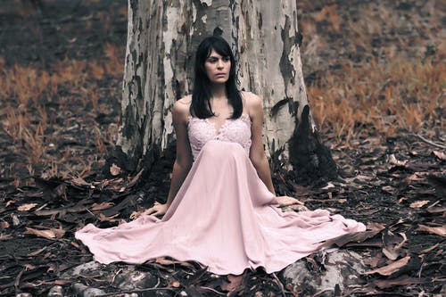 黑发女人坐在树前的粉红色无袖连衣裙的浅焦点摄影 · 免费素材图片