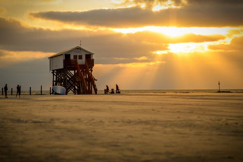 白云和橙色的天空下采取的海滩上的白色救生员房子 · 免费素材图片