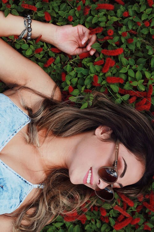 蓝钱布雷意大利面条皮带穿着太阳镜与红色花朵背景的女人 · 免费素材图片