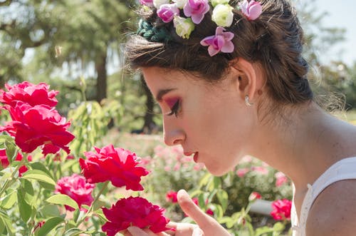 在红色的花朵上嗅到的花头饰的女人 · 免费素材图片