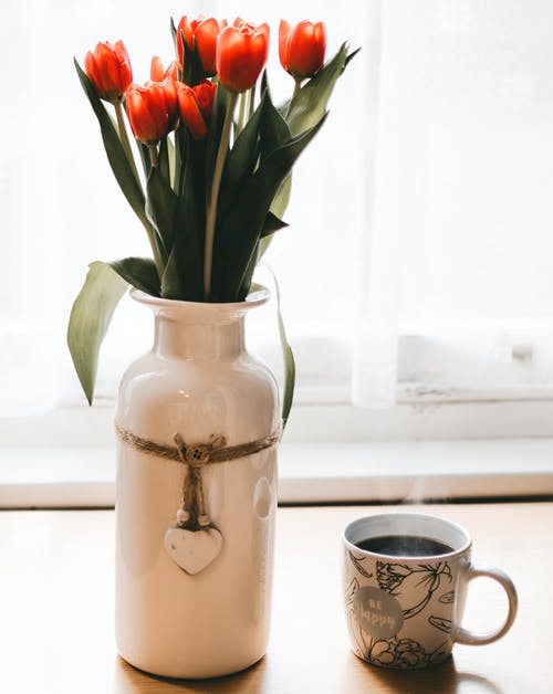 在咖啡旁边的白色陶瓷花瓶中的红色郁金香花 · 免费素材图片