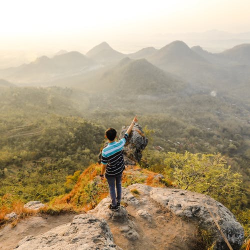 站在岩石山上指出山的人的照片 · 免费素材图片